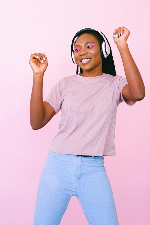 a woman with headphones standing in front of a pink wall, by Dulah Marie Evans, trending on pexels, happening, croptop, black teenage girl, wearing a light blue shirt, celebrating