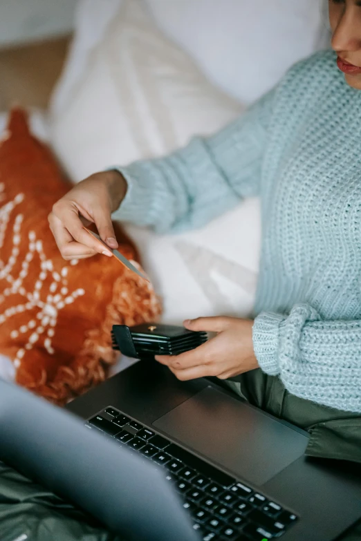 a woman sitting on a bed using a laptop computer, by Adam Marczyński, trending on pexels, happening, blue sweater, scanning items with smartphone, movie clip, seasonal