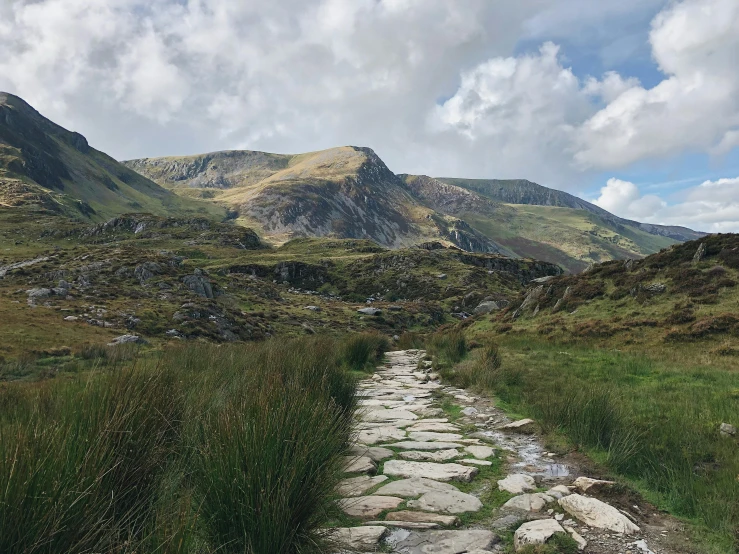 a stone path in a grassy area with mountains in the background, by Bedwyr Williams, unsplash contest winner, les nabis, wales, paved, slate, slide show