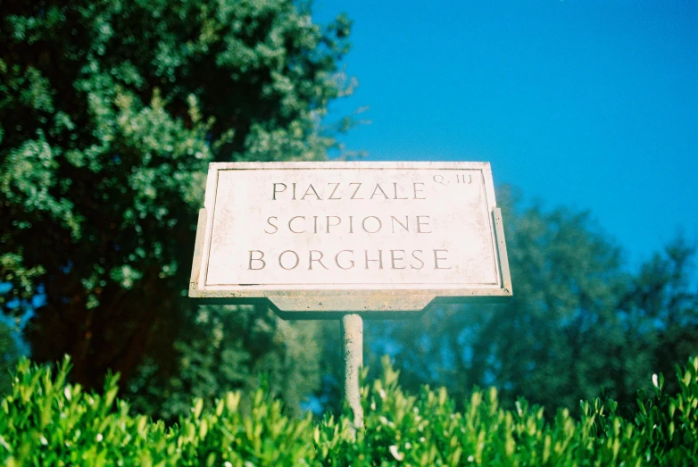 a white sign sitting on top of a lush green field, inspired by Francesco Bonsignori, baroque, taken with kodak portra, sunny sky, plaza, sienna