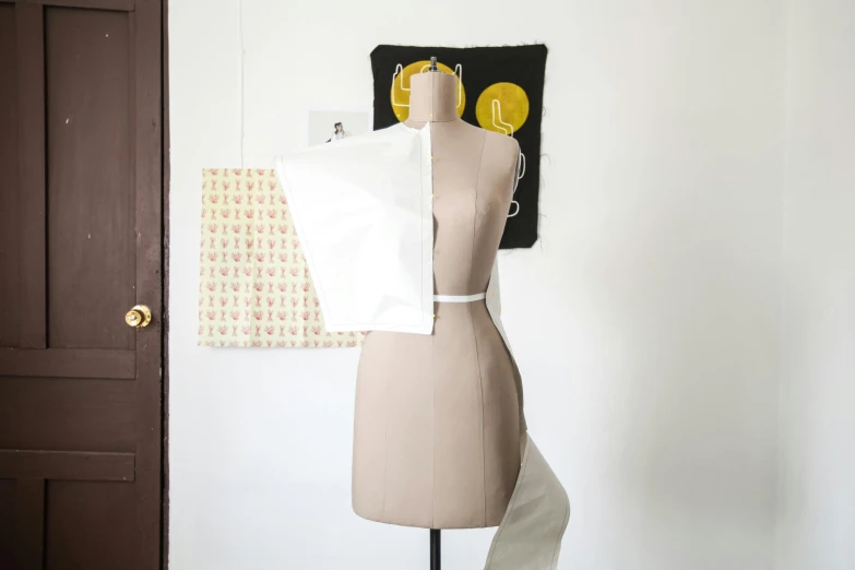 a mannequin sitting on top of a wooden table, an album cover, inspired by Esaias Boursse, unsplash, white apron, showing her shoulder from back, white wall coloured workshop, plastic and fabric