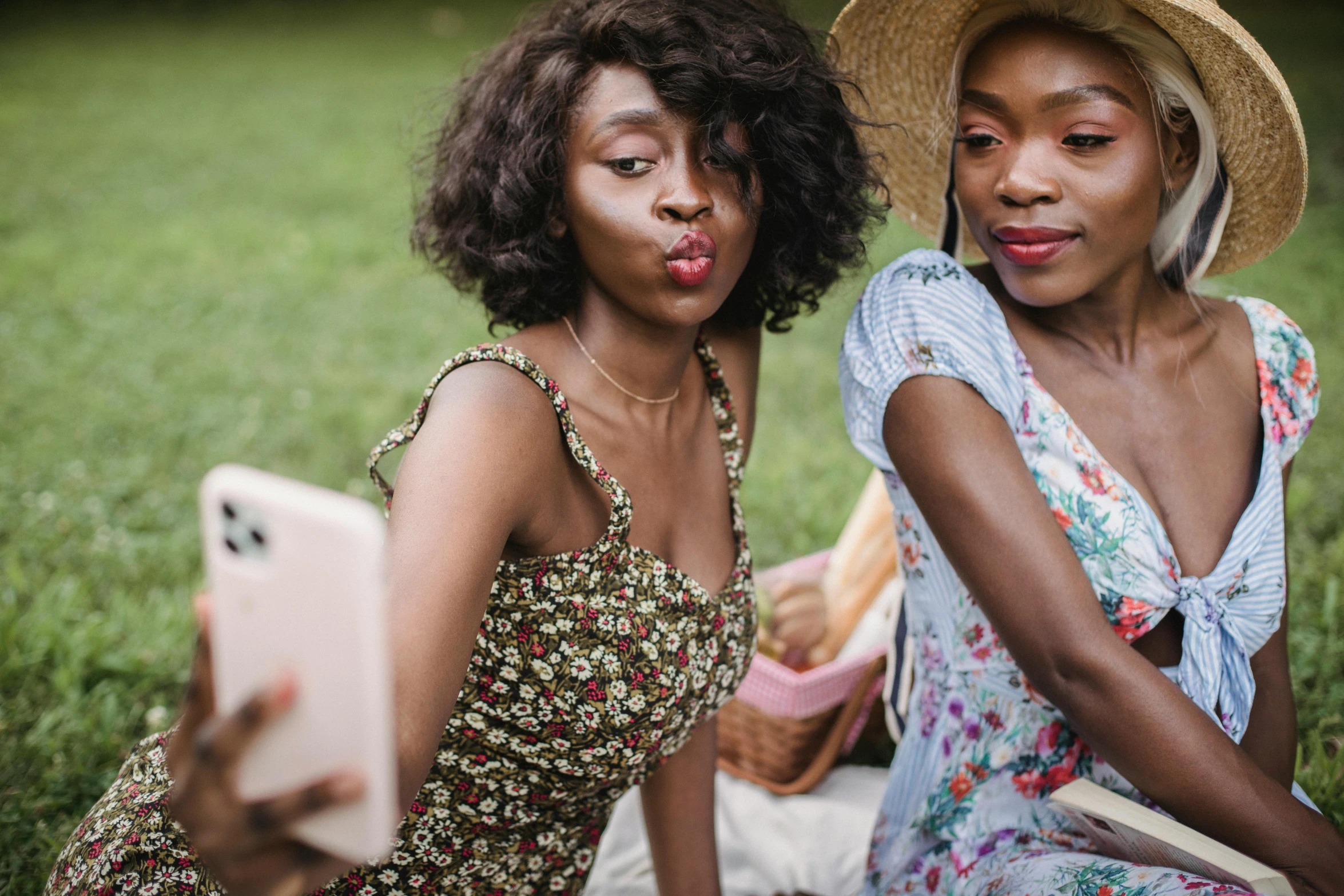 a couple of women sitting on top of a grass covered field, trending on pexels, happening, with brown skin, focus on pursed lips, people on a picnic, accidentally taking a selfie