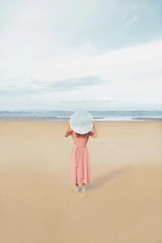 a woman standing on a beach holding an umbrella, inspired by Oleg Oprisco, unsplash contest winner, conceptual art, white straw flat brimmed hat, little planet, minimal pink palette, facing away