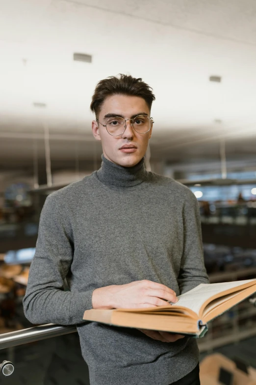 a man standing in a library holding a book, a character portrait, pexels contest winner, wearing turtleneck, handsome young man, glasses |, gif