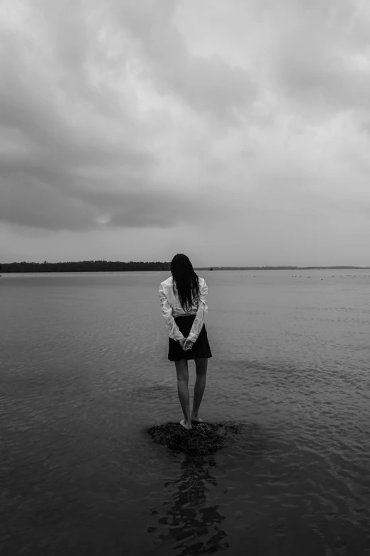 a woman standing in the middle of a body of water, a black and white photo, unsplash, sad sky, beautiful lonely girl, concert, unhappy