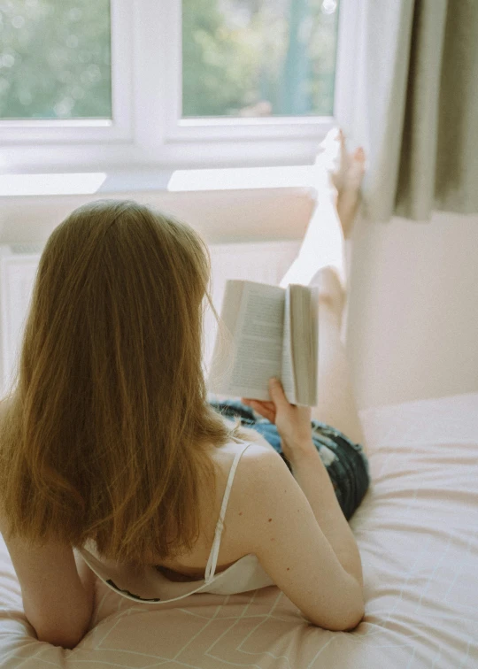 a woman laying on a bed reading a book, inspired by Elsa Bleda, pexels contest winner, back facing, gif, full body angle, extremely pale