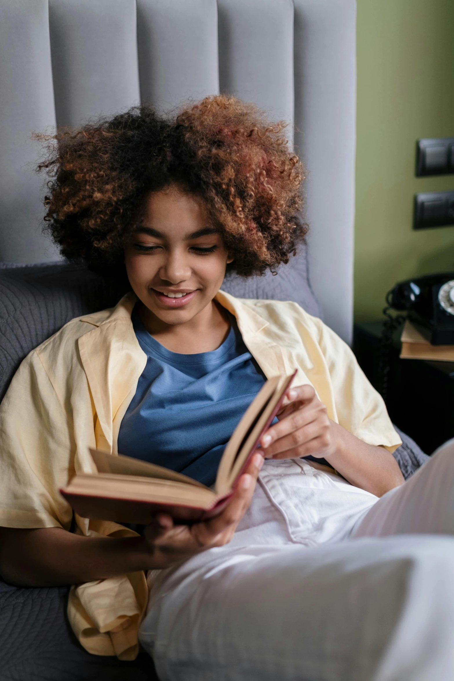 a woman sitting in a chair reading a book, pexels contest winner, happening, black teenage boy, laying in bed, fully functional, reading engineering book