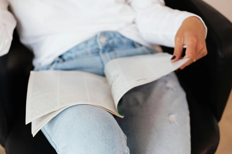 a woman sitting in a chair reading a book, trending on unsplash, private press, white shirt and blue jeans, reading a newspaper, thighs close up, sustainable materials