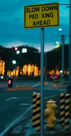 a yellow and black sign sitting on the side of a road, inspired by Elsa Bleda, unsplash, street lamps with orange light, set on singaporean aesthetic, teal lights, unfocused