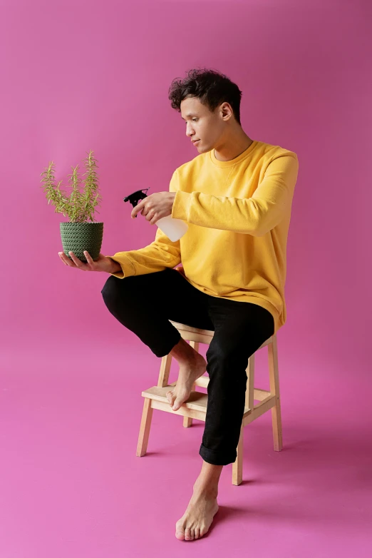 a man sitting on a chair holding a potted plant, trending on pexels, magic realism, pink and yellow, wearing casual sweater, model standing pose, non binary model