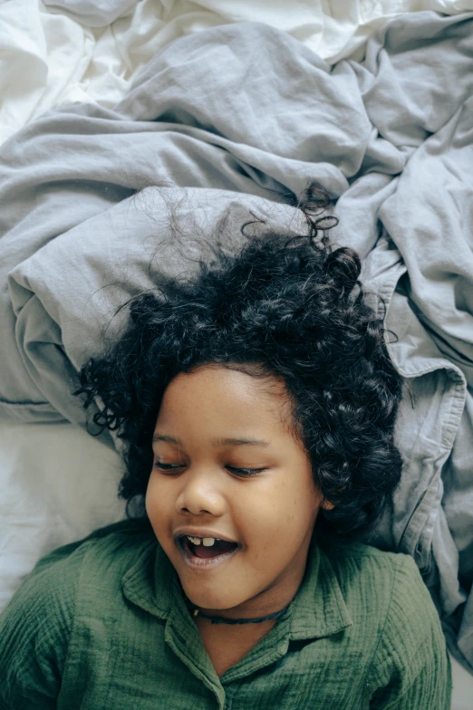 a small child laying on top of a bed, pexels contest winner, happening, black curly hair, head bent back in laughter, trending on vsco, curled up under the covers