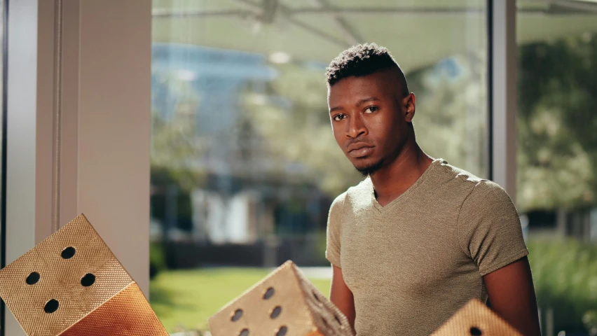 a man standing next to a pile of cardboard blocks, pexels contest winner, brown skin man egyptian prince, looking outside, 2 1 savage, carrying a tray