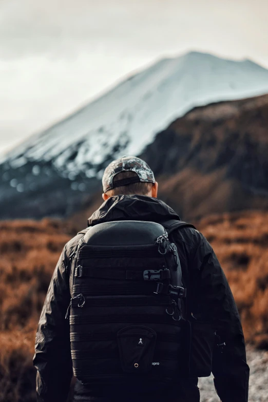 a man with a backpack standing in front of a mountain, trending on unsplash, black tactical gear, new zealand, instagram picture, slightly pixelated