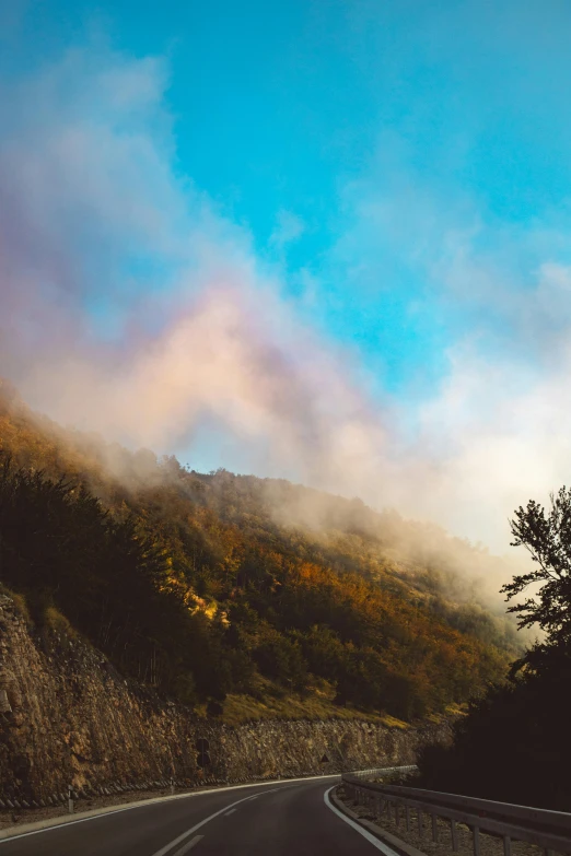 a car driving down the road on a foggy day, pexels contest winner, romanticism, colorful ravine, chile, burning clouds, hill with trees