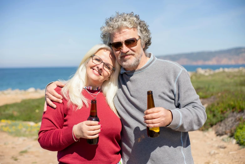 a man and a woman standing next to each other, a photo, by Bertram Brooker, pexels, renaissance, holding a bottle of beer, seaview, short white beard, amber glasses