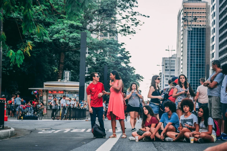 a group of people sitting on the side of a street, by Amelia Peláez, pexels contest winner, happening, avenida paulista, avatar image, performing, panoramic view of girl