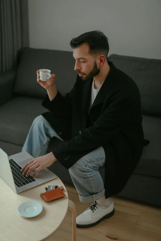 a man sitting on a couch using a laptop, by Sebastian Vrancx, pexels contest winner, drinking tea, standing, serious look, man in black