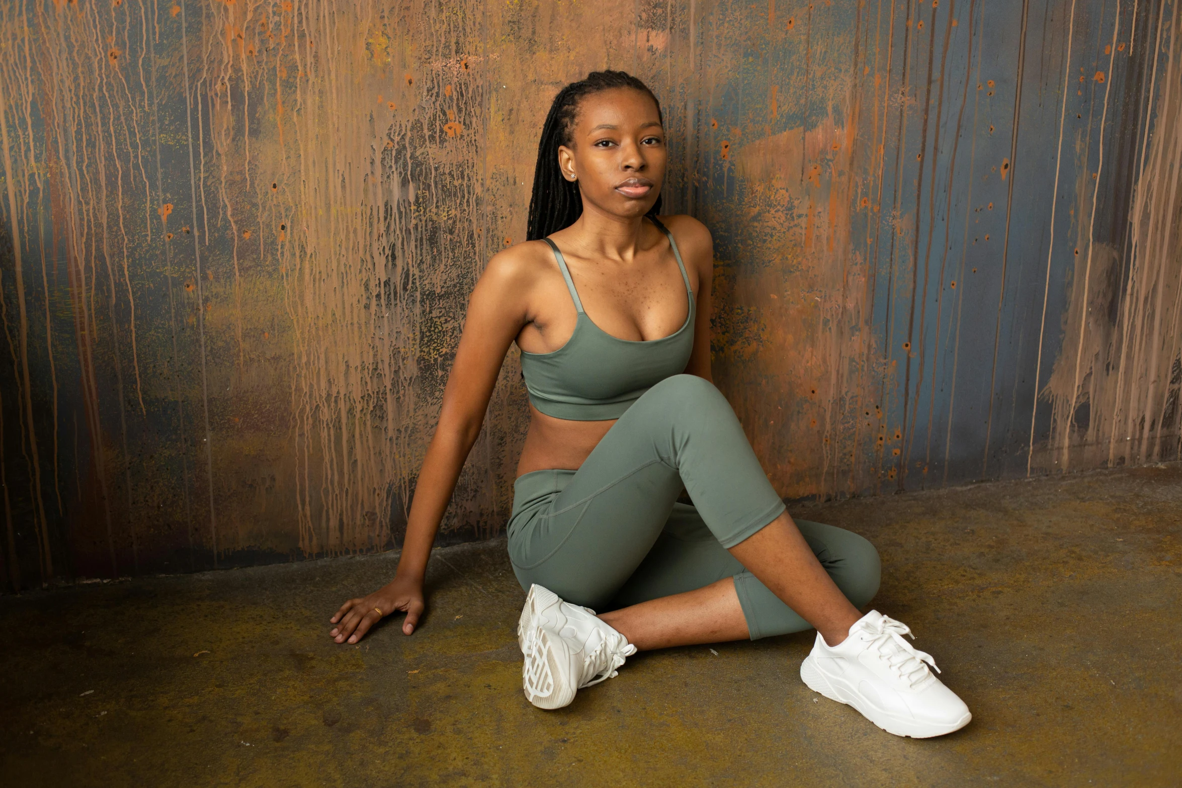 a woman in a sports bra top and leggings sitting on the floor, inspired by Esaias Boursse, pexels contest winner, muted green, dark skinned, full body image, leaning against the wall