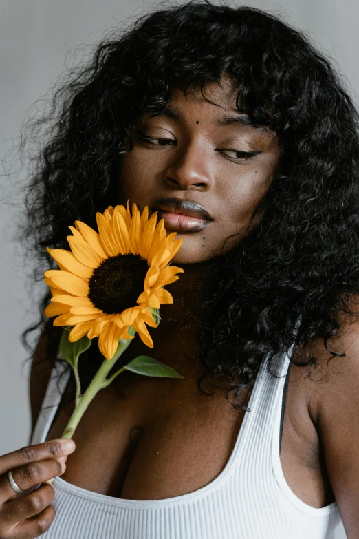 a woman holding a sunflower in front of her face, an album cover, trending on pexels, a black man with long curly hair, alluring plus sized model, ( ( dark skin ) ), non binary model