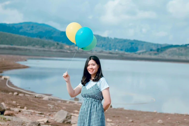 a woman standing in front of a lake holding a bunch of balloons, inspired by Kim Jeong-hui, pexels contest winner, dilraba dilmurat, vietnamese woman, avatar image, sunny day time