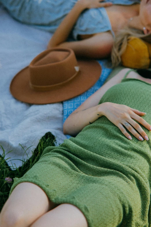 a couple of women laying on top of a grass covered field, by Carey Morris, trending on pexels, renaissance, green hat, hands behind back, people on a picnic, subdued color