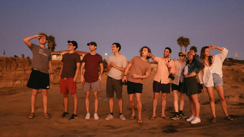 a group of people standing on top of a sandy beach, by Ryan Pancoast, with red haze and a massive grin, los angelos, wearing shorts, 3 am