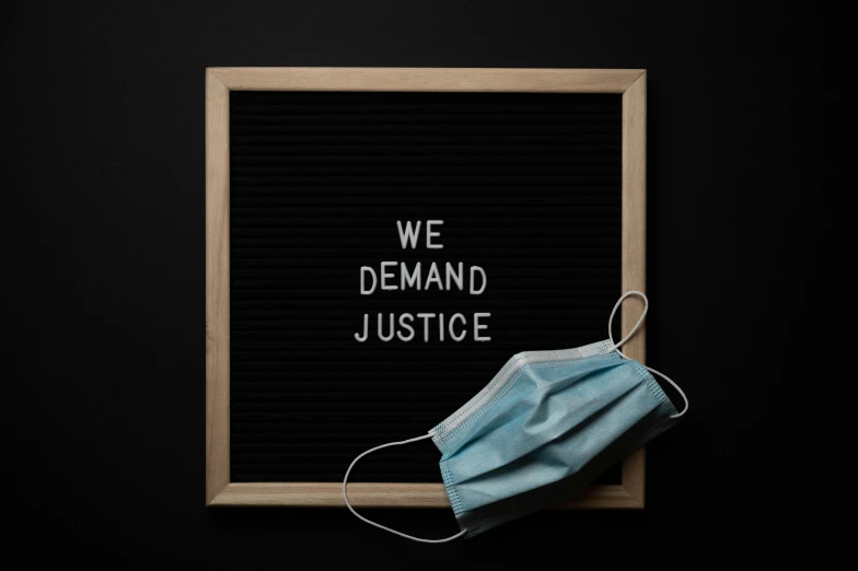 a mask on top of a sign that says we demand justice, a picture, trending on pexels, blackboard, background image, profile picture, 1