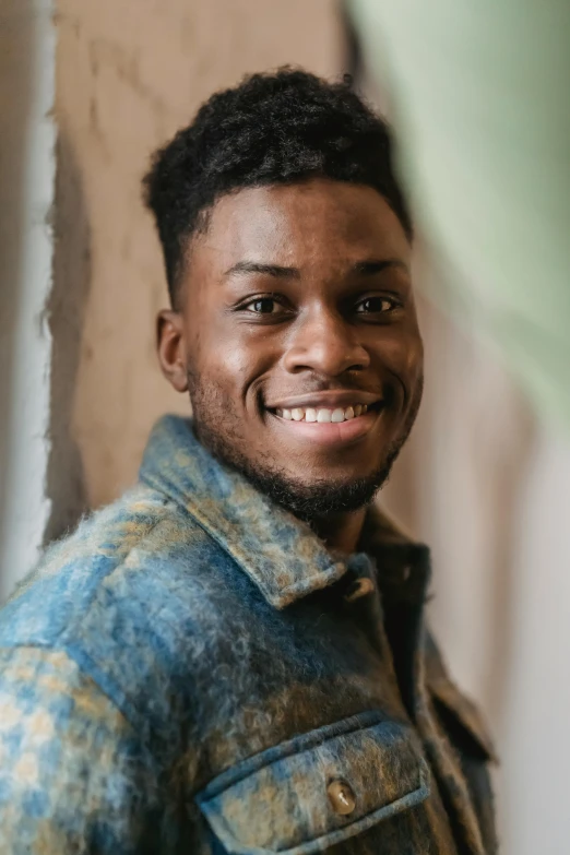 a close up of a person wearing a jacket, by Stokely Webster, he is smiling, young man, with textured hair and skin, maria borges