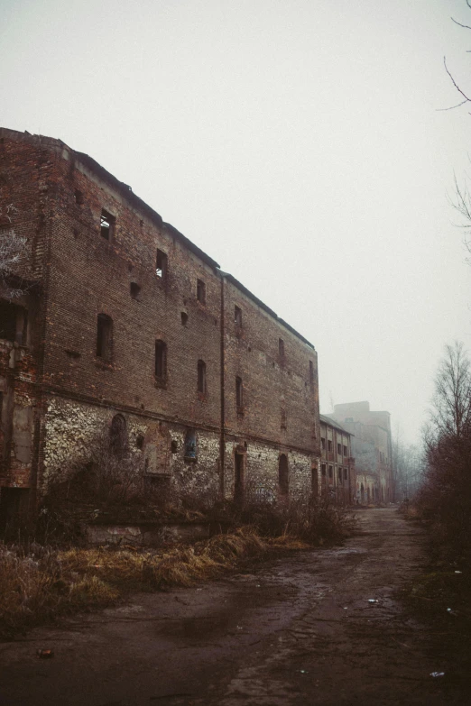 an old brick building sitting on the side of a road, inspired by Elsa Bleda, pexels contest winner, renaissance, ominous foggy environment, soviet yard, ruins landscape, barracks