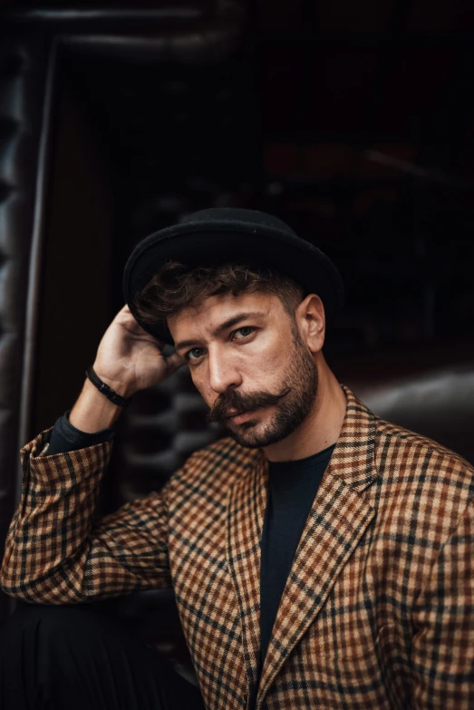 a man sitting in a chair with a hat on, an album cover, inspired by Germán Londoño, trending on pexels, renaissance, androgynous face, mark edward fischbach, portrait pose, artem chebokha