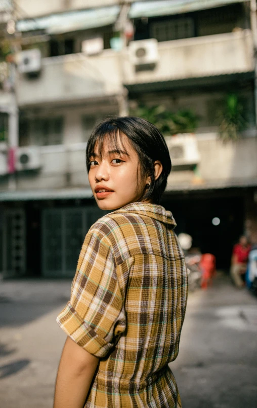 a woman standing in the middle of a street, by Tan Ting-pho, trending on pexels, realism, wearing plaid shirt, side portrait rugged girl, square, yellow hue