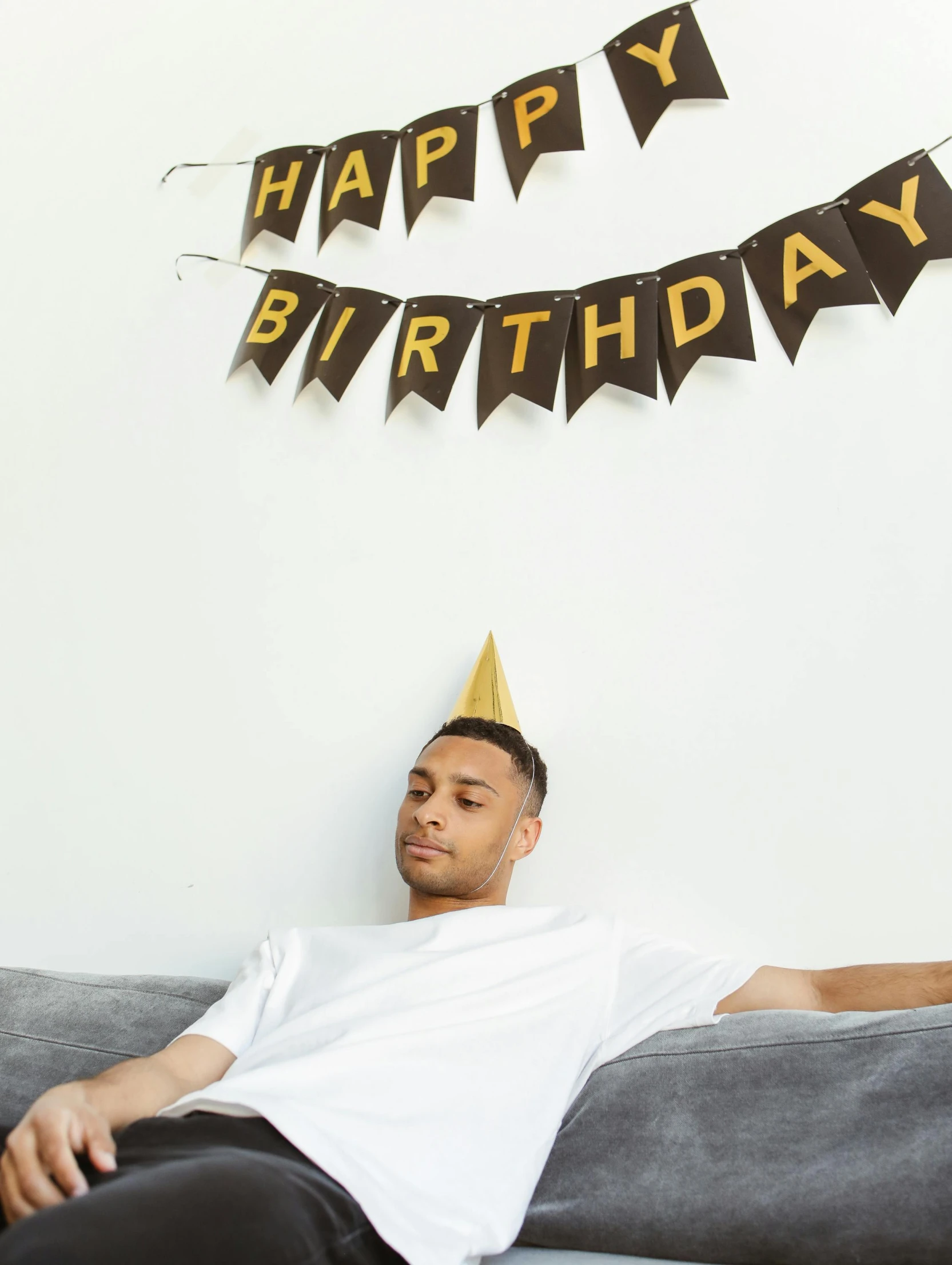 a man sitting on a couch wearing a party hat, trending on unsplash, happy birthday, laying on a bed, black crown, thumbnail