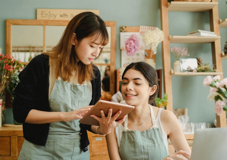 two women working on a laptop in a flower shop, by Aya Goda, trending on pexels, arts and crafts movement, avatar image, holding a clipboard, of taiwanese girl with tattoos, ( waitress ) girl