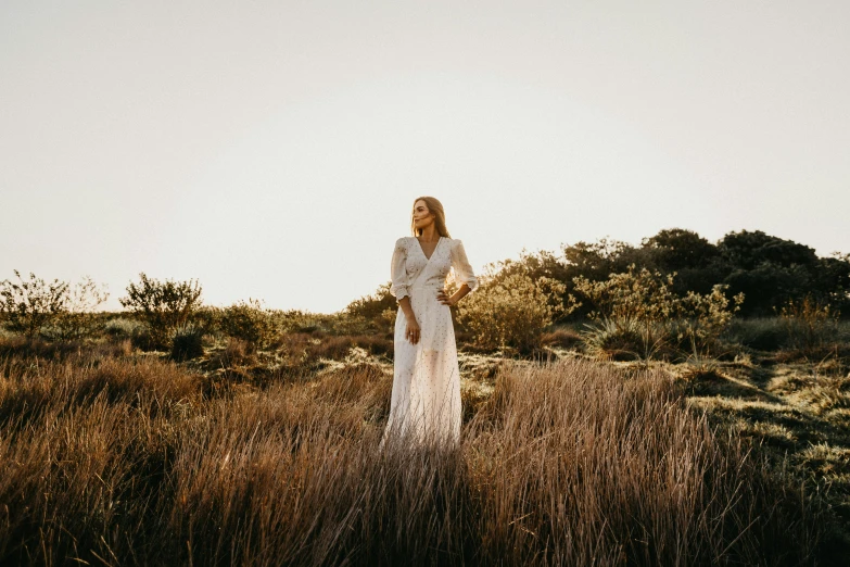 a woman in a white dress standing in a field, an album cover, unsplash, coastal, evening light, cinematic outfit photo, various posed