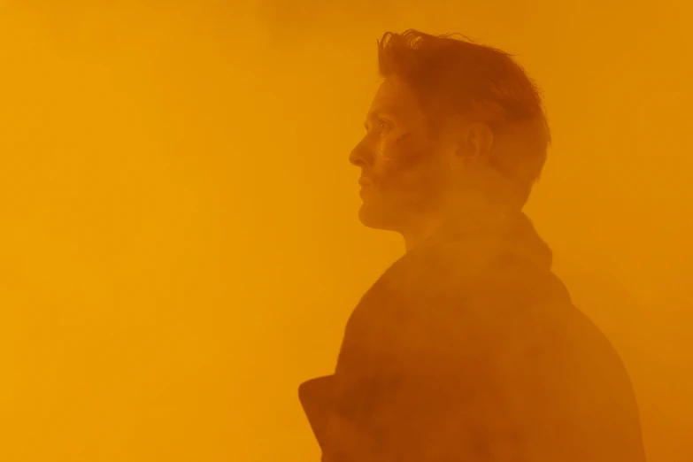 a man standing in front of a yellow background, inspired by roger deakins, orange fog, jeremy renner, shot from the side, **cinematic