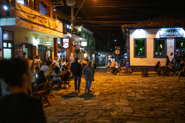 a group of people walking down a cobblestone street, by Alejandro Obregón, happening, local bar, scenic view at night, thumbnail, colombia