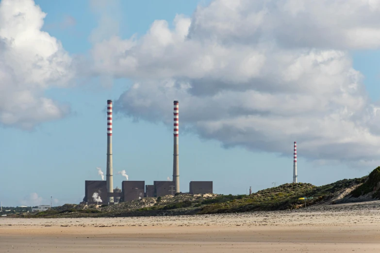 a man flying a kite on top of a sandy beach, by Matthias Stom, pexels contest winner, plasticien, smokestacks, electrical plant location, seen from a distance, bartlomiej gawel