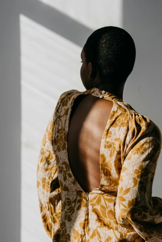 a woman standing in front of a white wall, inspired by Marià Fortuny, trending on unsplash, renaissance, wearing yellow floral blouse, open back dress, african american woman, in the morning light