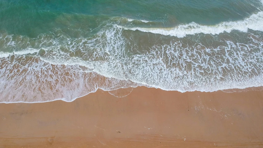 a person riding a surfboard on top of a sandy beach, bird view, 5 feet away, the ocean, wave