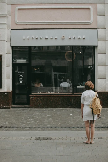 a woman walking down a sidewalk in front of a store, pexels contest winner, renaissance, polish hyper - casual, white building, facing away, bakery
