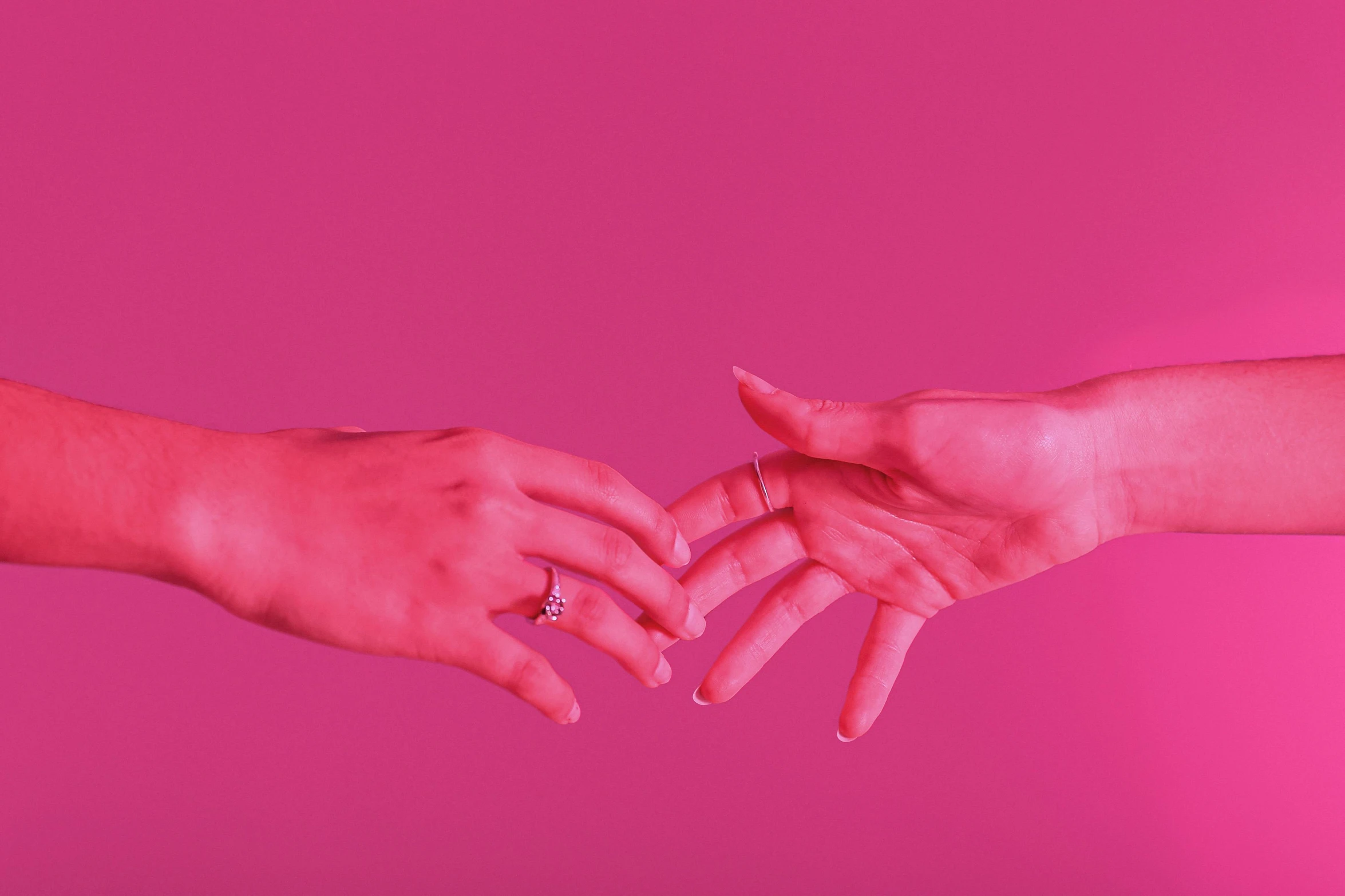 two hands holding each other in front of a pink background, rubies, reaching out to each other, looking towards camera, deep colour