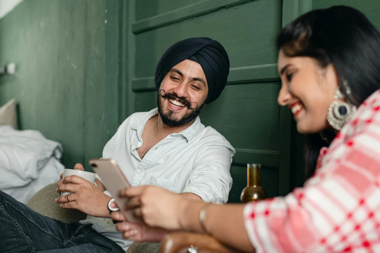 a man in a turban sitting next to a woman, inspired by Manjit Bawa, trending on pexels, happening, holds a smart phone in one hand, happy friend, in a pub, avatar image