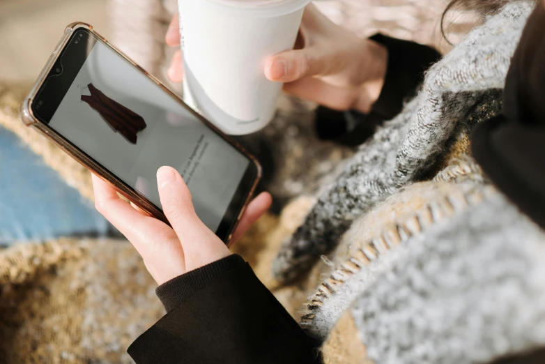 a woman holding a cup of coffee and a cell phone, trending on pexels, smart textiles, instagram post, a cold, 1 4 9 3