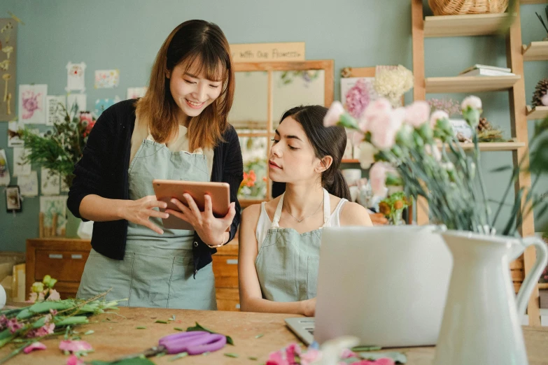 two women in a flower shop looking at a tablet, trending on pexels, avatar image, ruan jia and brom, professional image, looking her shoulder