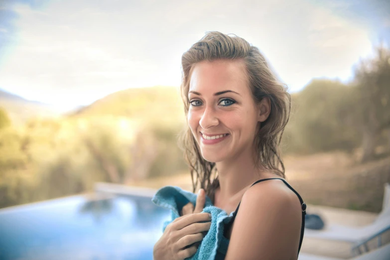 a beautiful young woman standing next to a swimming pool, pexels contest winner, happening, lovingly looking at camera, wearing a towel, nature outside, smiling slightly