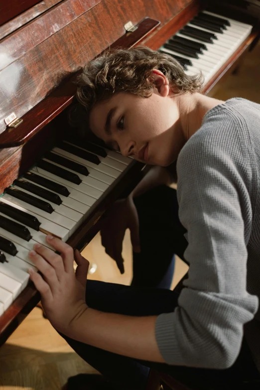 a young man sitting in front of a piano, trending on pexels, photorealism, joe keery, sleepy feeling, high angle, ignant