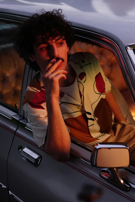 a man sitting in a car smoking a cigarette, an album cover, inspired by Nan Goldin, trending on pexels, renaissance, patterned clothing, long twirling moustache, finn wolfhard, graphic tees