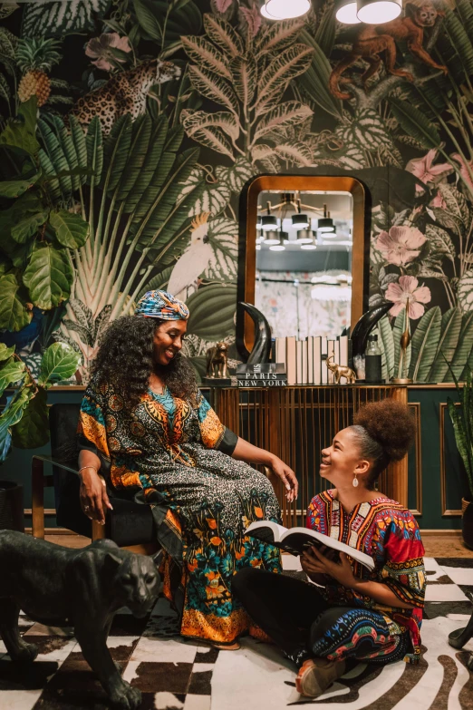 a woman sitting in a chair next to a black dog, a portrait, afrofuturism, floral jungle treehouse, two women, in opulent library, portrait featured on unsplash