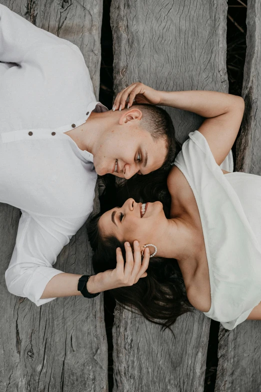 a man and a woman laying on a wooden floor, wearing a white button up shirt, bride and groom, looking down from above, hand on cheek