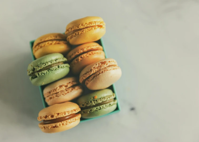 a box of macarons sitting on top of a table, a colorized photo, by Emma Andijewska, trending on pexels, muted color, chartreuse and orange and cyan, thumbnail, halo halo halo halo 8k